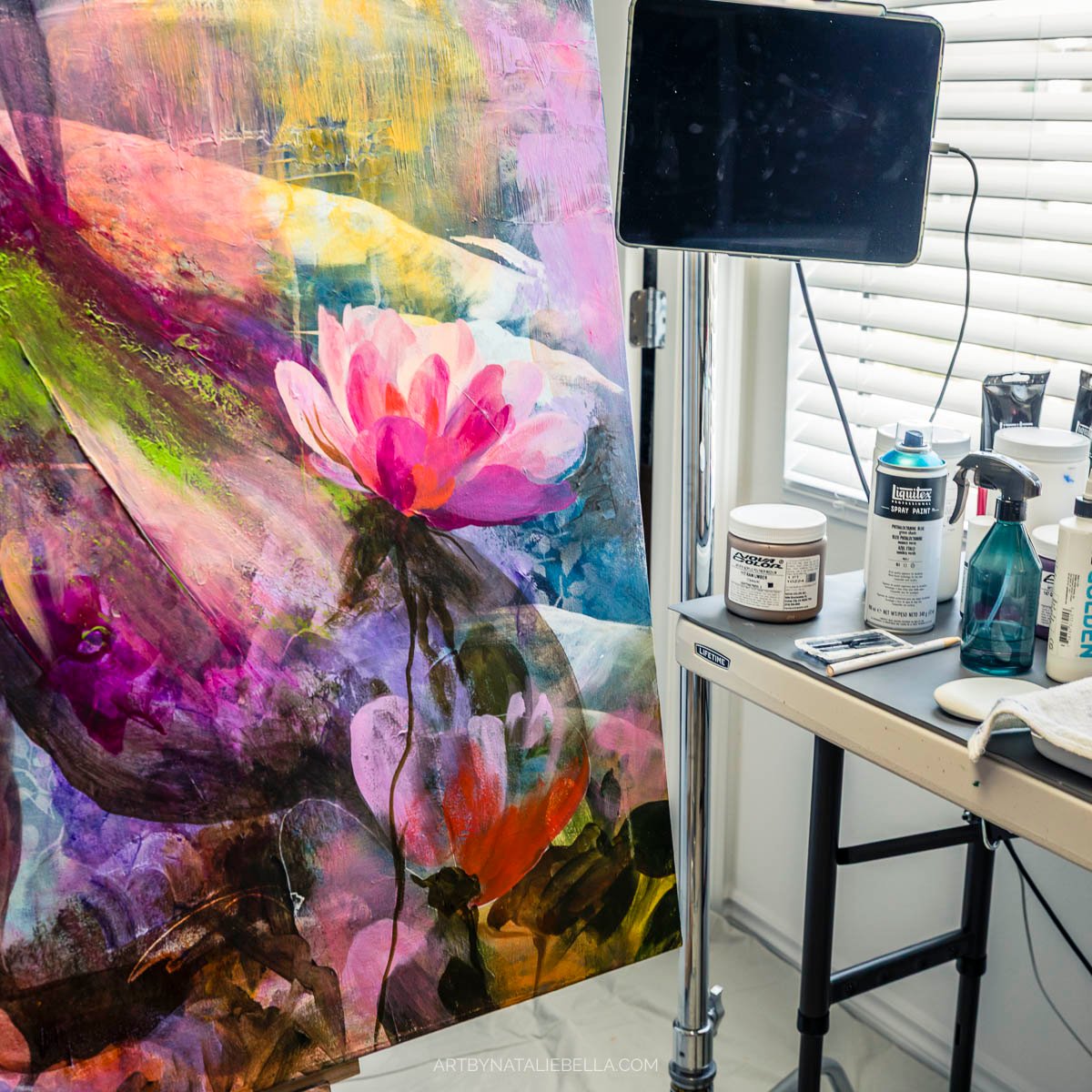Artist studio workspace showing 48x48 inch mixed media painting in progress with floral motifs and art supplies