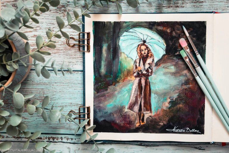 Gouache painting study of woman with umbrella displayed in open watercolor sketchbook with paintbrushes and eucalyptus on rustic wooden background, artist studio setup