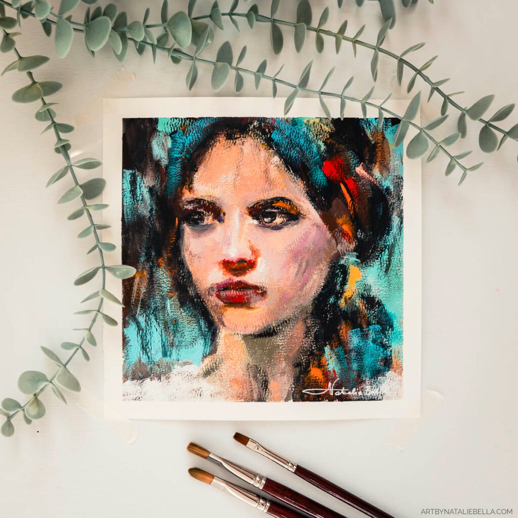 Styled flat lay featuring the gouache painting 'Unguarded' on a cream background, beautifully framed by delicate eucalyptus branches at the top and three fine artist brushes with wooden handles at the bottom. The 8x8 inch portrait on watercolor paper shows a woman with striking eyes and red lips painted in vibrant turquoise, orange, and warm flesh tones. The natural styling elements complement the organic, expressive brushwork of the portrait, creating an elegant presentation that showcases both the artwork and the artist's tools.