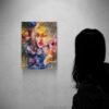Silhouetted woman viewing colorful mixed media portrait painting with textured flowers and golden light on gallery wall - She Chose Light by Las Vegas artist Natalie Bella