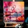 Coastal Grace, 24x24 inch oil and mixed media painting by Natalie Bella displayed on wooden easel showing two flamingos in tropical setting with pink florals